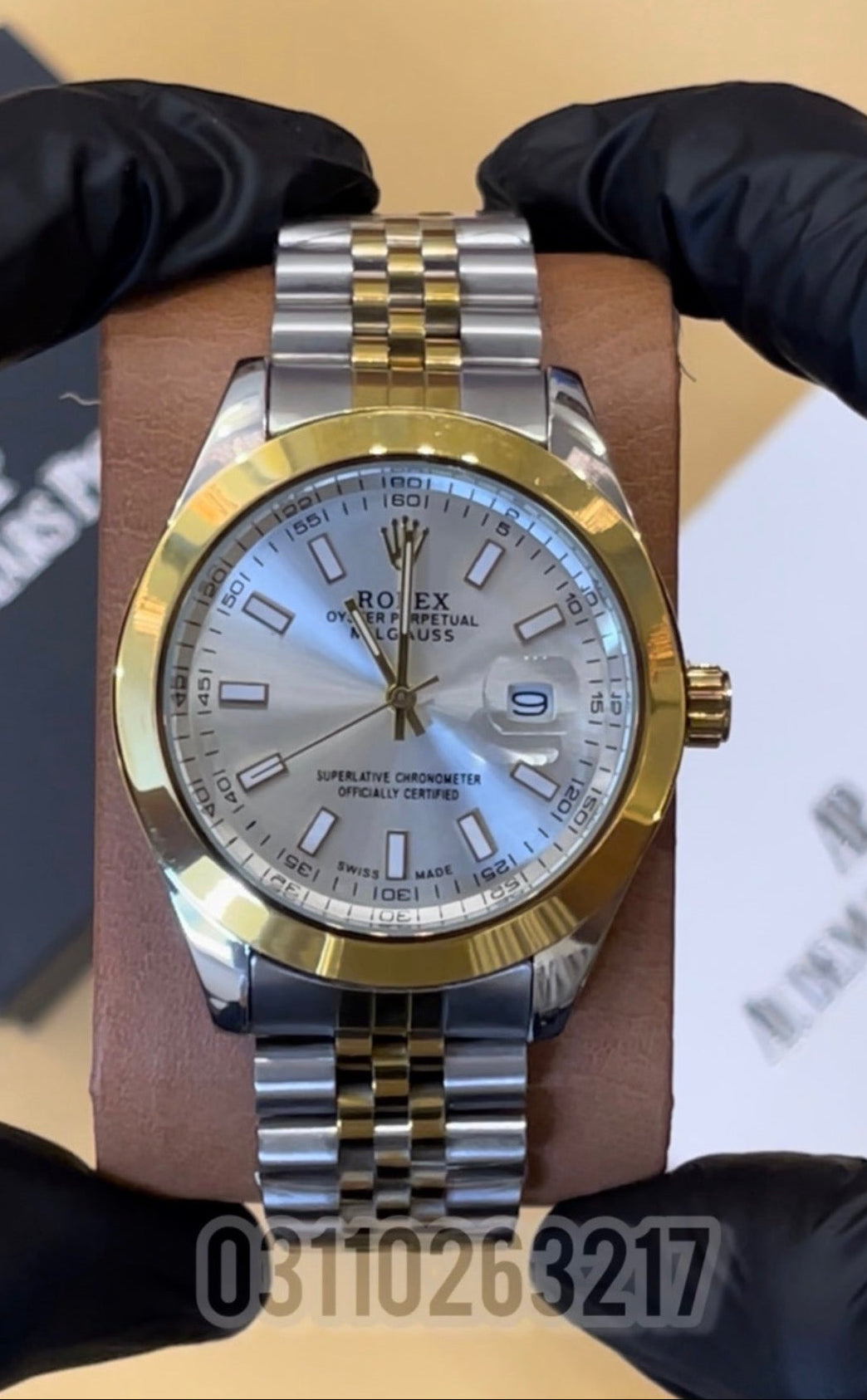 Gold and silver watch held by a gloved hand with a blurred background